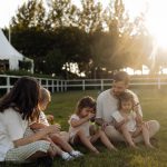 Family sitting on grass enjoying leisure time outdoors, with sun setting in the background.